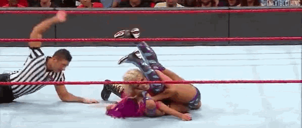 two women are wrestling in a wrestling ring with a referee .