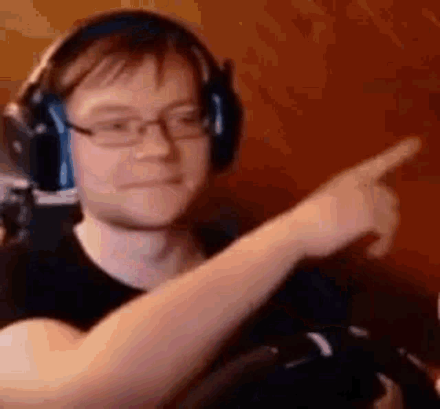 a man wearing headphones and glasses is pointing his finger at something .