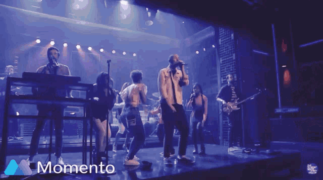 a group of people singing on a stage with the word momento in the lower right corner