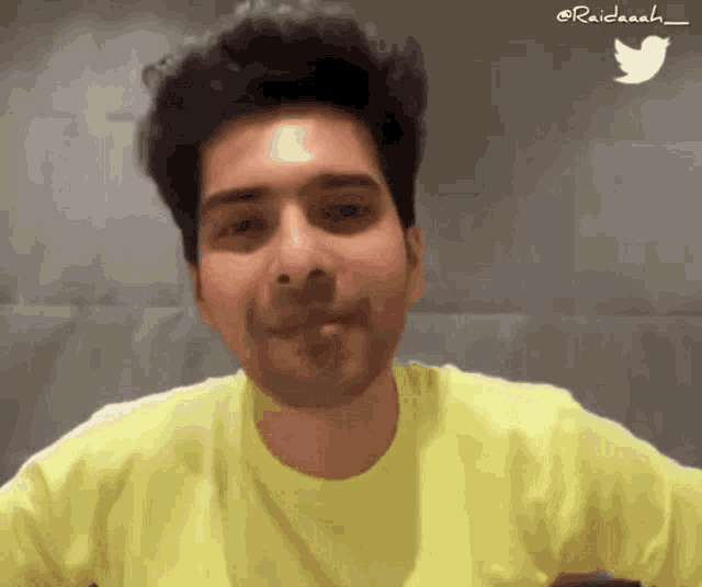 a man wearing a yellow t-shirt is smiling with a twitter icon in the background