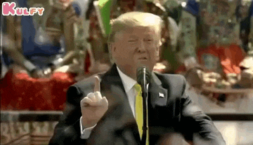 donald trump is giving a middle finger while speaking into a microphone .
