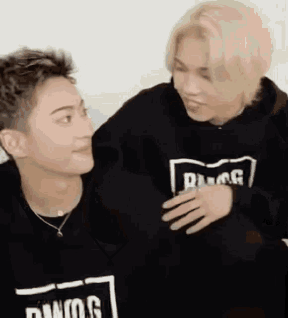 two young men are hugging each other and looking at each other . one of the men is wearing a black hoodie .