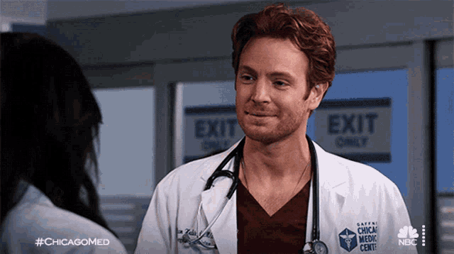 a man in a lab coat with a stethoscope around his neck stands in front of a sign that says exit only