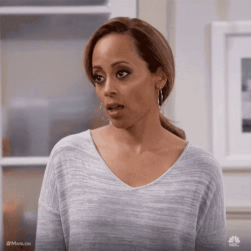 a woman in a grey sweater and hoop earrings is making a funny face .