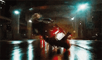 a person is riding a red motorcycle down a wet street at night .