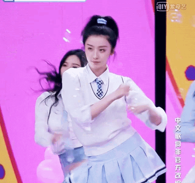 a girl in a white sweater and blue pleated skirt is standing next to another girl