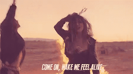 a woman is dancing in front of a fire with the words come on make me feel alive .