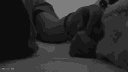 a black and white photo of a couple holding hands in bed .