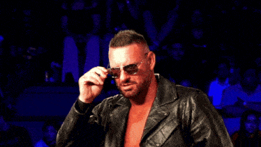 a man wearing sunglasses and a leather jacket stands in front of a crowd