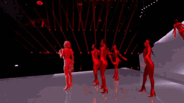 a woman is singing into a microphone while a group of dancers are dancing around her