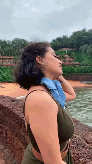 a woman wearing a scarf around her neck is standing on a rock near the water .