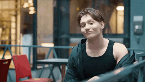 a man wearing a black tank top and a black jacket is sitting at a table and smiling .
