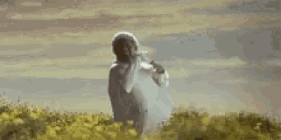 a man in a white robe is standing in a field with his arms outstretched .