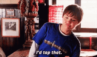a young boy in a blue shirt is sitting at a table and saying `` i 'd tap that '' .