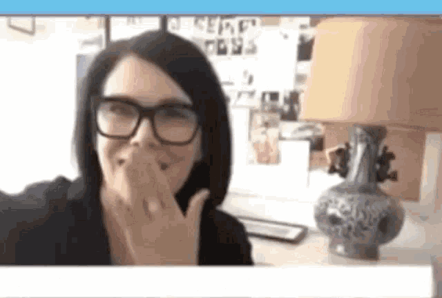 a woman wearing glasses is smiling and covering her mouth with her hand .
