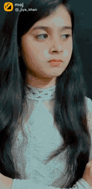 a girl with long dark hair is wearing a white shirt and a moji sticker