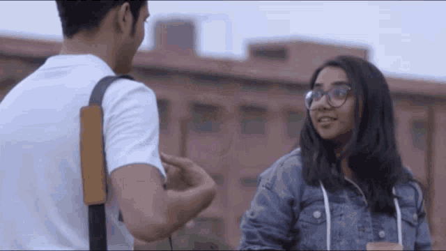 a man and a woman are standing next to each other and talking . the woman is wearing glasses .