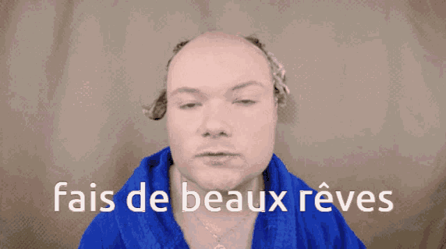 a bald man wearing a blue robe says " fais de beaux reves " in white letters