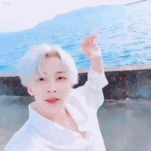 a young boy with white hair is standing in front of the ocean