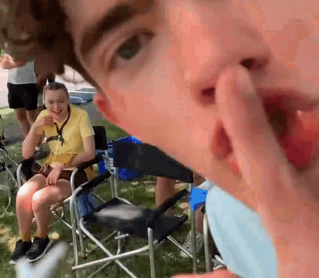 a girl in a yellow shirt is sitting in a folding chair while a man holds his nose