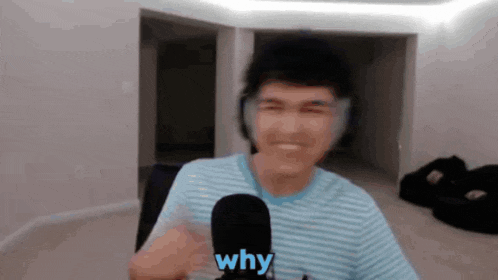 a man wearing headphones is talking into a microphone and the word why is on the screen behind him