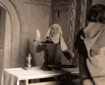 a nun is standing in front of a table with a cross on it and laughing .