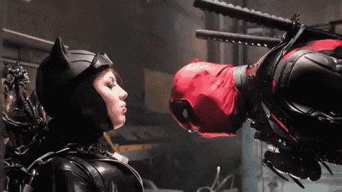 a woman in a catwoman costume kisses a man in a deadpool suit