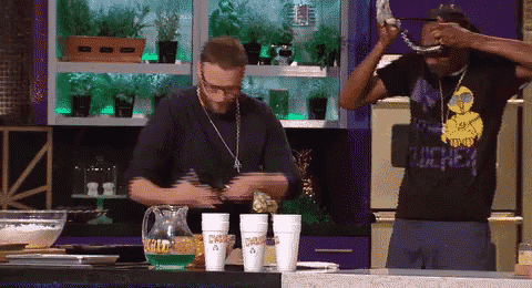 a man wearing a black shirt that says ' snoop dogg ' on it stands in a kitchen