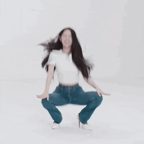 a woman in a white t-shirt and blue jeans is squatting down .