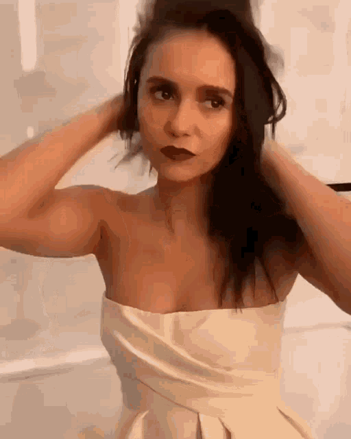 a woman in a strapless white dress is holding her hair in a bun .