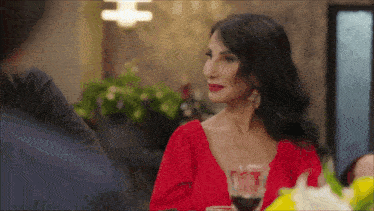 a woman in a red top is sitting at a table with a glass of wine