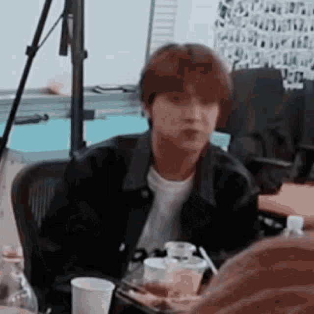 a man in a black jacket is sitting at a table with a plate of food .