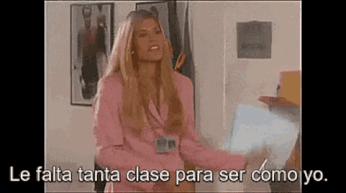 a woman in a pink suit is standing in front of a sign that says le falta tanta clase para ser como yo