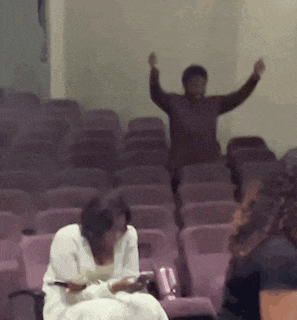 a group of people are sitting in a row of purple chairs with their arms in the air
