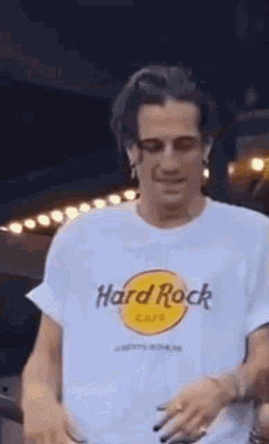 a man wearing a white hard rock cafe t-shirt is standing in front of a building .