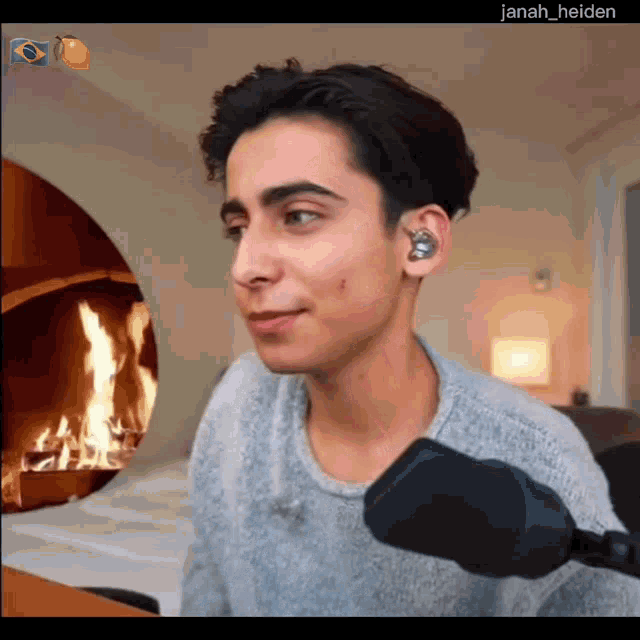 a young man sitting in front of a microphone with a fireplace in the background