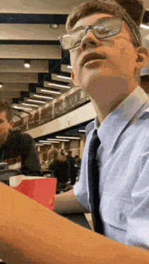 a boy wearing glasses and a tie is sitting at a table in a cafeteria .