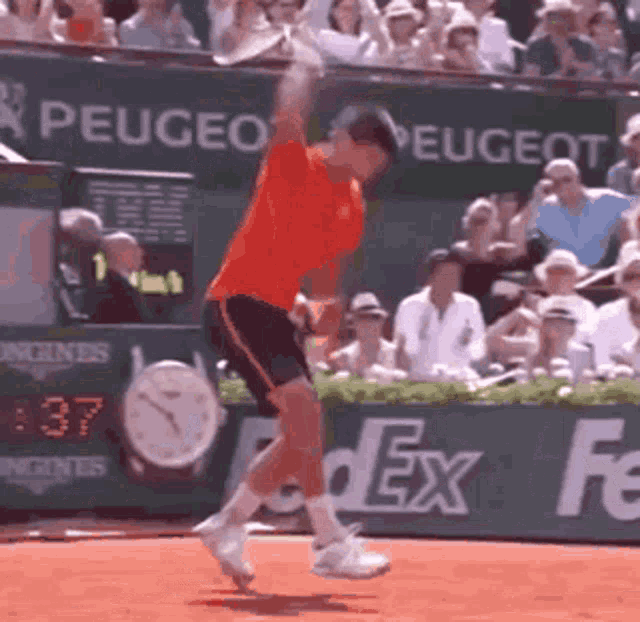 a man in an orange shirt is swinging a tennis racket on a tennis court