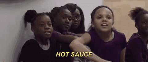 a group of young girls are standing next to each other and one of them is holding a bottle of hot sauce .