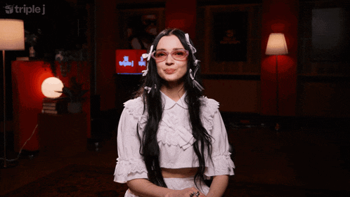 a woman wearing glasses and a white top stands in front of a triple j sign