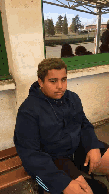 a boy in a blue jacket is sitting on a bench