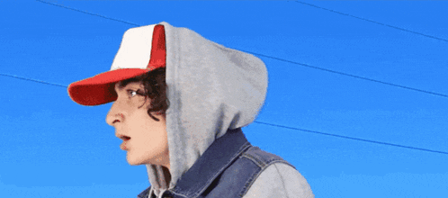 a man with curly hair wearing a hat and hoodie