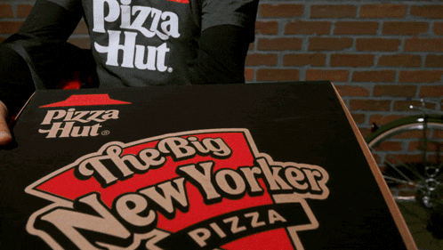 a person wearing a pizza hut shirt is holding a box of the big new yorker pizza