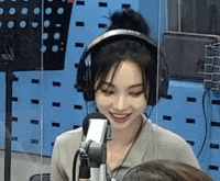 a woman wearing headphones is smiling in front of a microphone in a room .