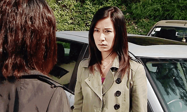 a woman in a trench coat stands next to another woman in a car