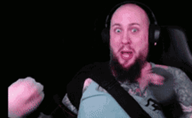 a man with a beard and tattoos is wearing headphones and holding a pink object in his hand .