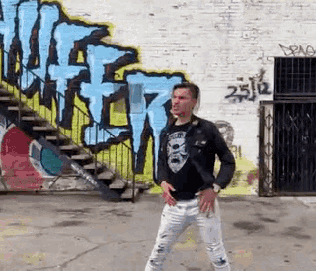 a man is standing in front of a wall with graffiti on it and stairs .