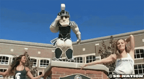 two women are dancing in front of a statue of a spartans warrior