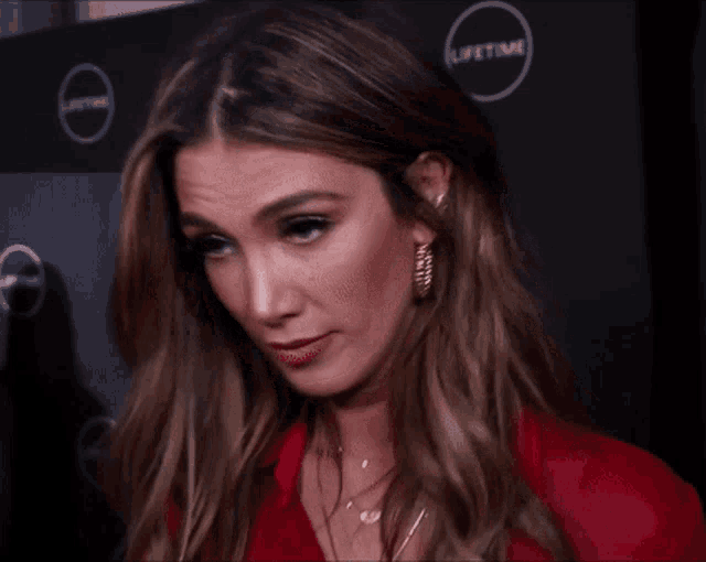 a woman in a red jacket and gold hoop earrings is making a funny face