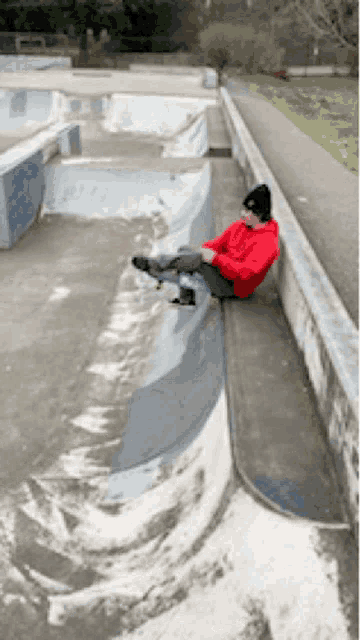 a person in a red hoodie sits on a ledge with a skateboard